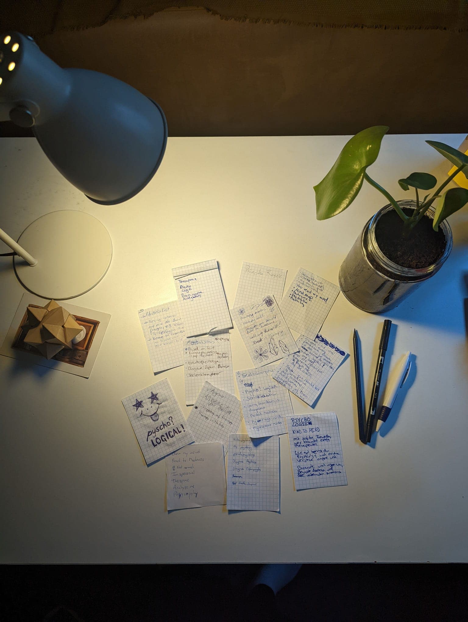 Ein weißer Schreibtisch mit Lampe, Pflanze und vielen kleinen Zetteln voller handgeschriebener psychologischer Notizen.