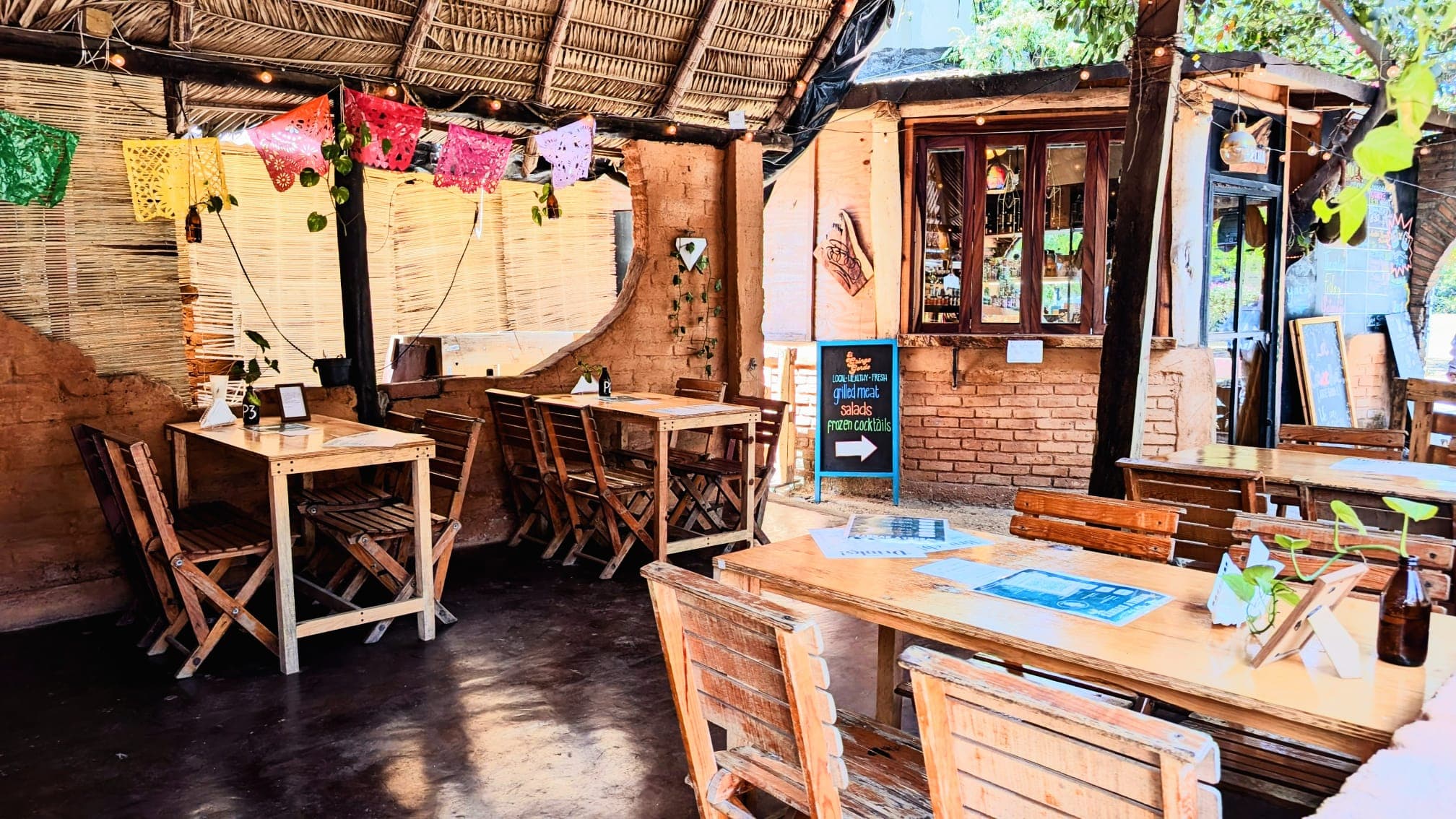 Ein gemütliches Restaurant im Freien mit Holztischen, Strohdach und farbenfrohen mexikanischen Papiergirlanden.